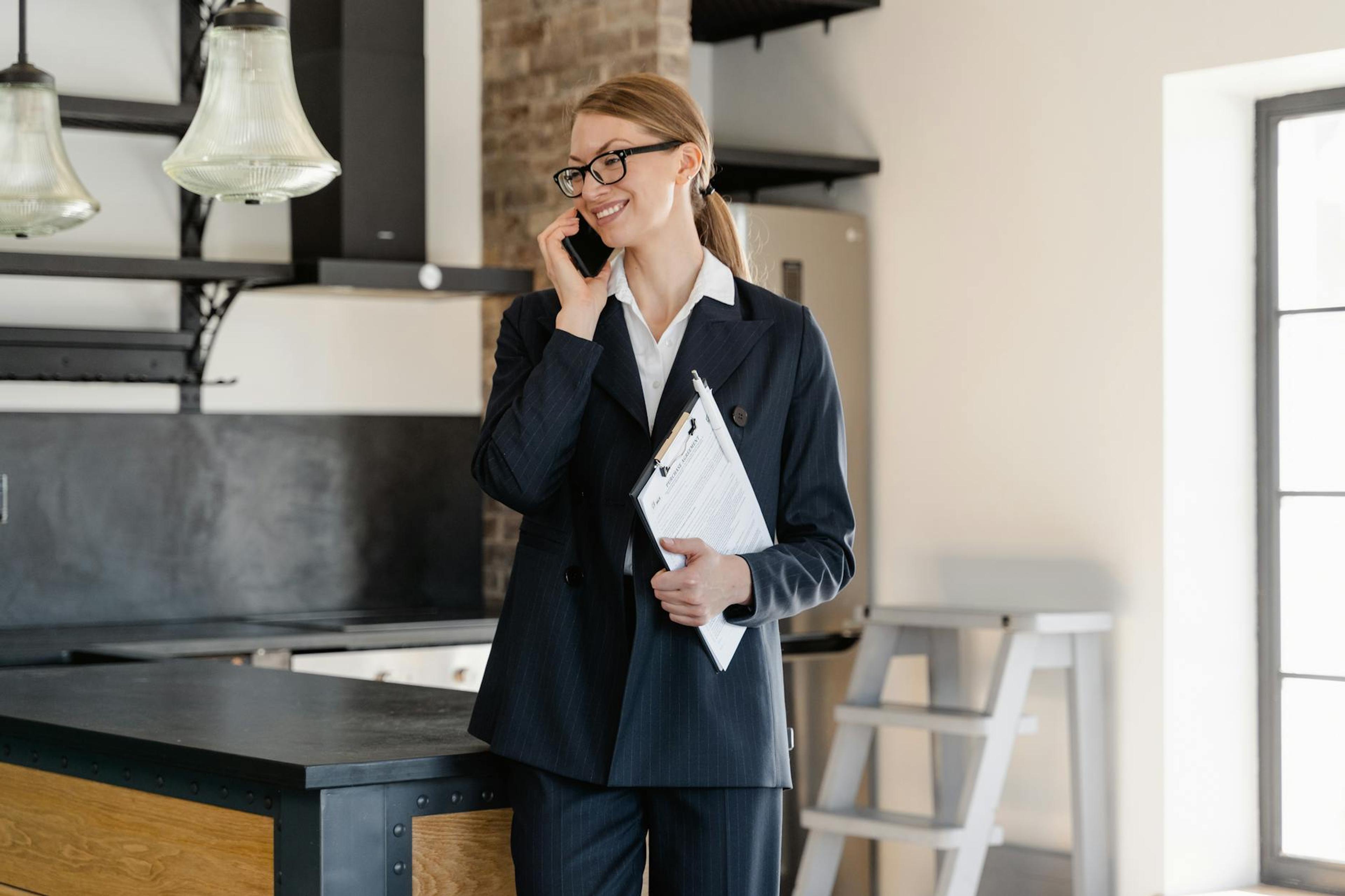 Confident businesswoman in office attire making a call while holding a clipboard in a modern workspace.