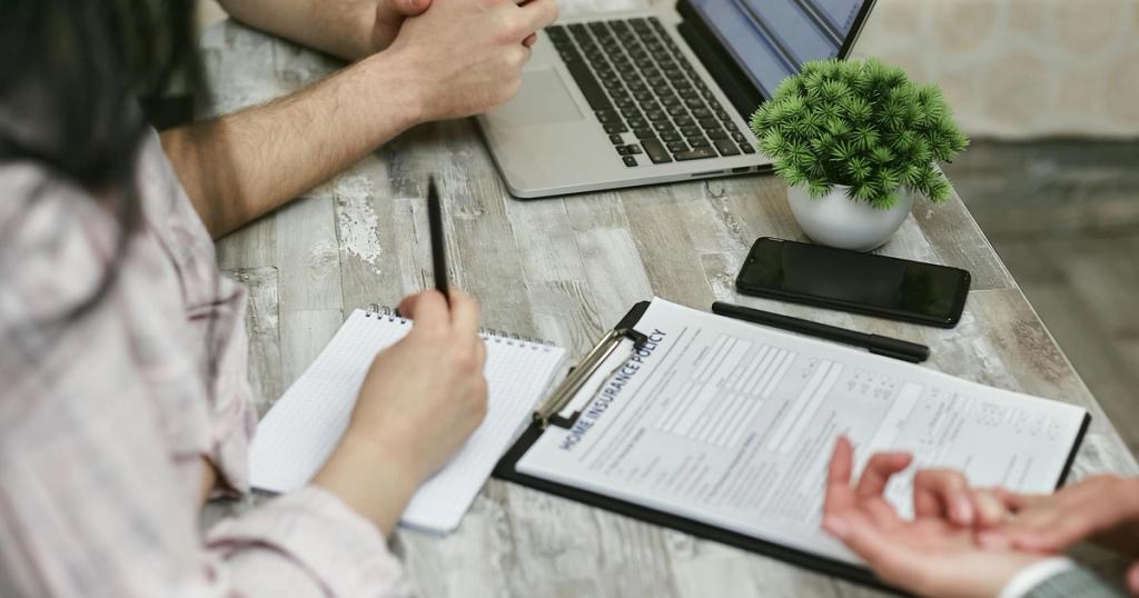 Professionals discussing home insurance policy over laptop and notes in an office setting.