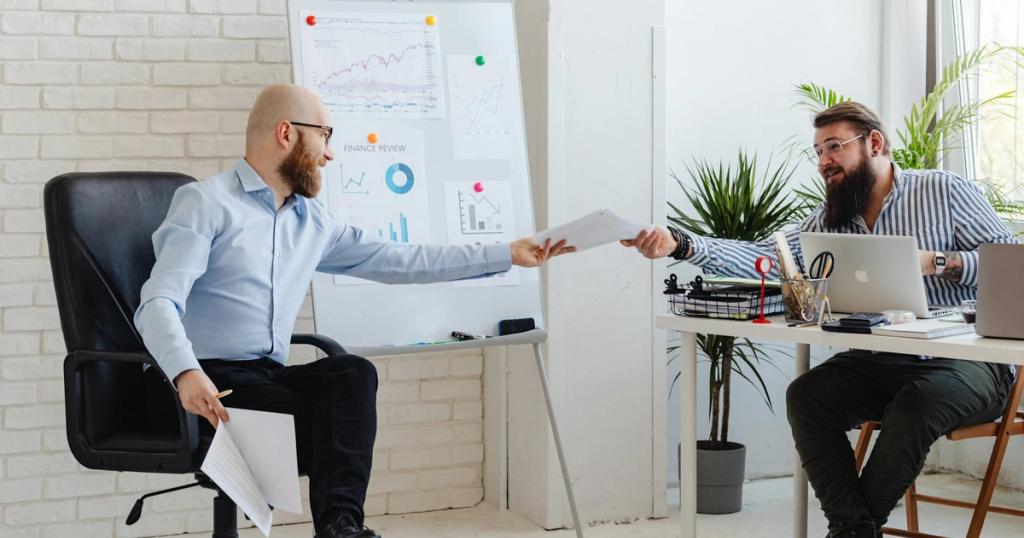 Two business professionals exchanging documents in a modern office setting with charts and graphs.