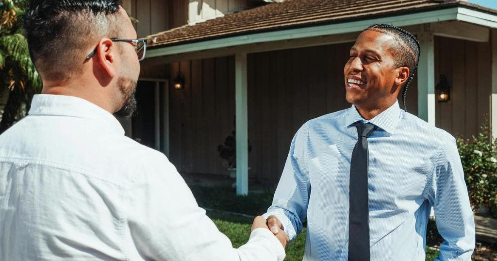 Two real estate professionals shaking hands in front of a new home during a transaction.