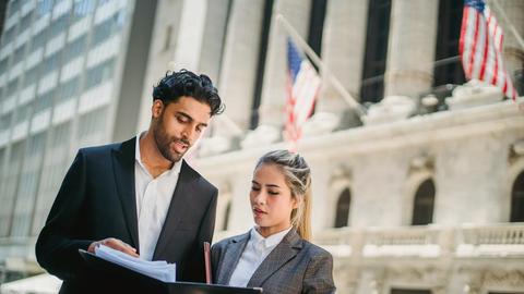 Two business professionals review documents outside a financial institution, indicating teamwork and collaboration.
