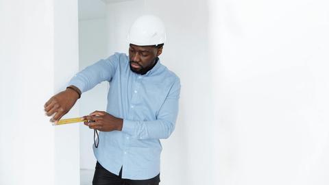 A man in a hard hat measures a wall, showcasing precision in a building interior.