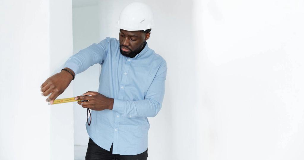 A man in a hard hat measures a wall, showcasing precision in a building interior.