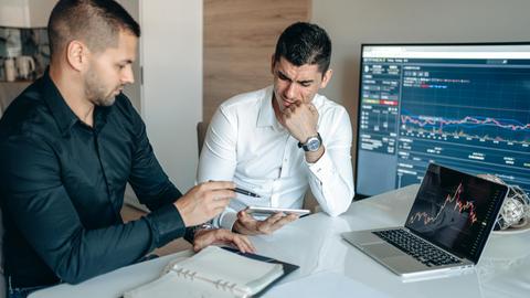 Two men discussing business analytics in an office with laptops and graphs.