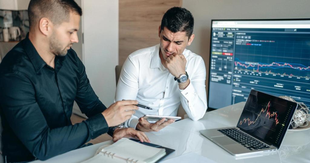 Two men discussing business analytics in an office with laptops and graphs.