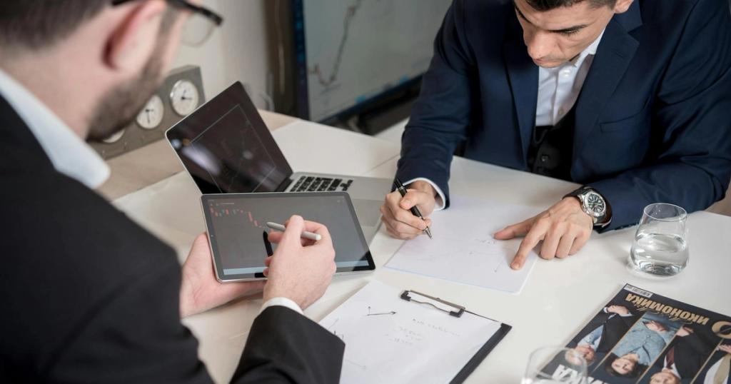 Two businessmen analyzing cryptocurrency market trends using a tablet and laptop in an office.