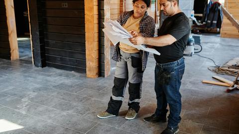 Two workers examining blueprints inside a building under construction, showcasing teamwork.