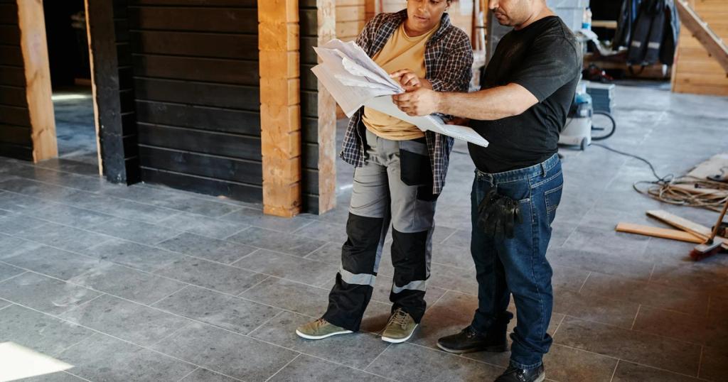 Two workers examining blueprints inside a building under construction, showcasing teamwork.