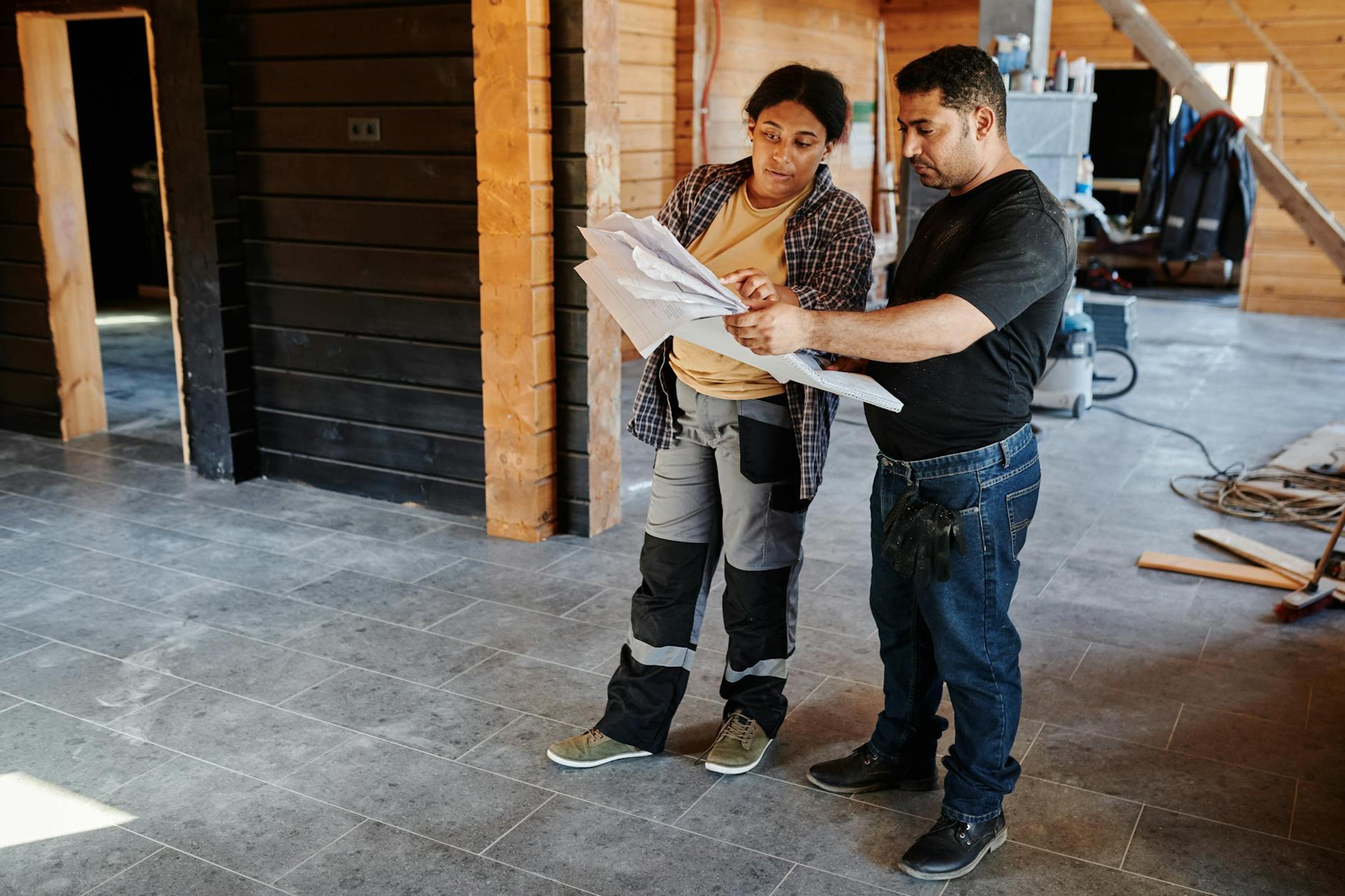 Two workers examining blueprints inside a building under construction, showcasing teamwork.