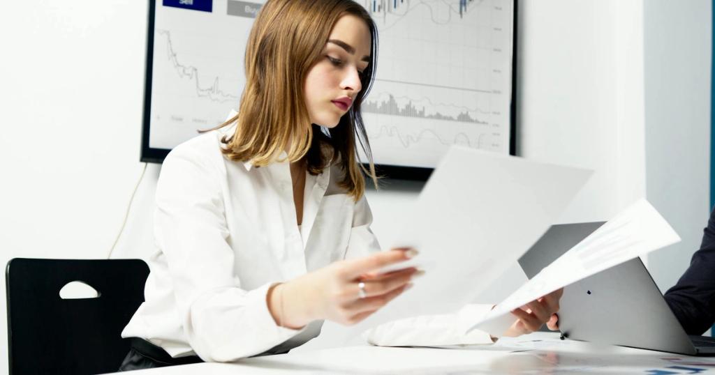 Focused woman analyzing financial reports in a modern office setting with charts and graphs.