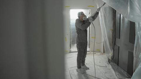 Man in protective gear spray painting a house's interior during renovation work.