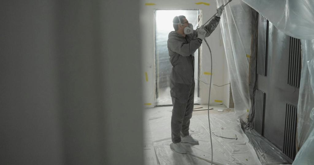 Man in protective gear spray painting a house's interior during renovation work.