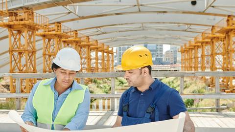 Engineering team analyzing blueprints together at an outdoor construction site with safety gear.