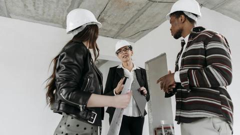 A diverse group of construction professionals wearing hard hats in a discussion at a building site.