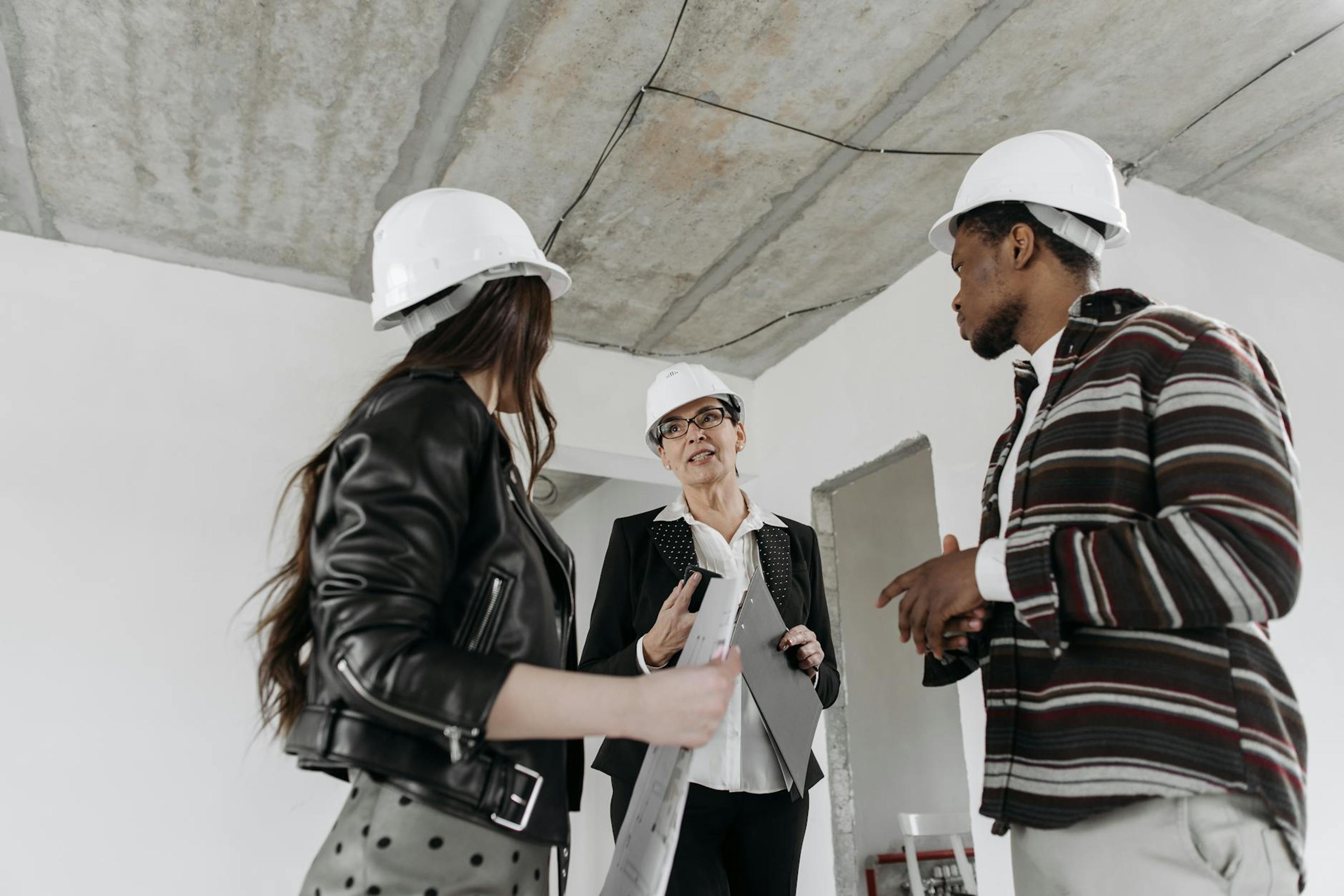 A diverse group of construction professionals wearing hard hats in a discussion at a building site.