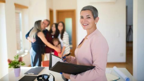 Confident real estate agent presents modern home to elated family, sealing the deal with a smile.
