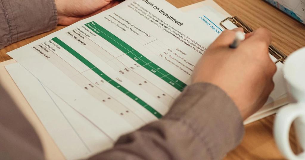 A person analyzing a return on investment report with a pen in hand on a desk.
