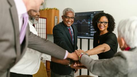 A diverse group of professionals celebrate a successful meeting indoors, showcasing teamwork and unity.