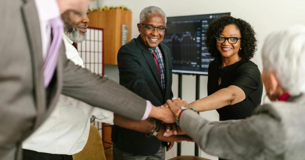 A diverse group of professionals celebrate a successful meeting indoors, showcasing teamwork and unity.