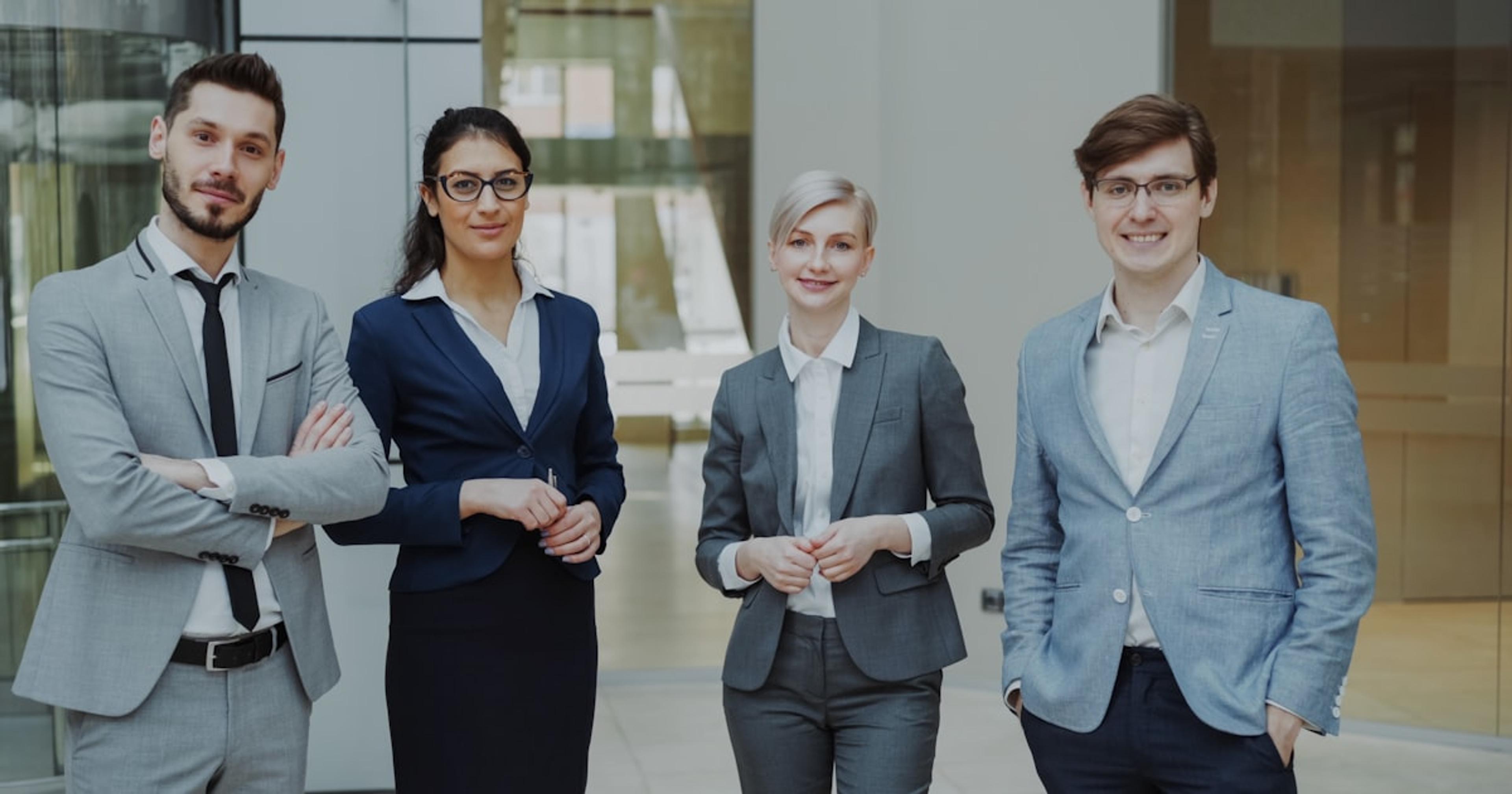 Four professionals in business attire stand together.