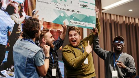Excited business team celebrates winning a ten thousand dollar prize at a tech conference.