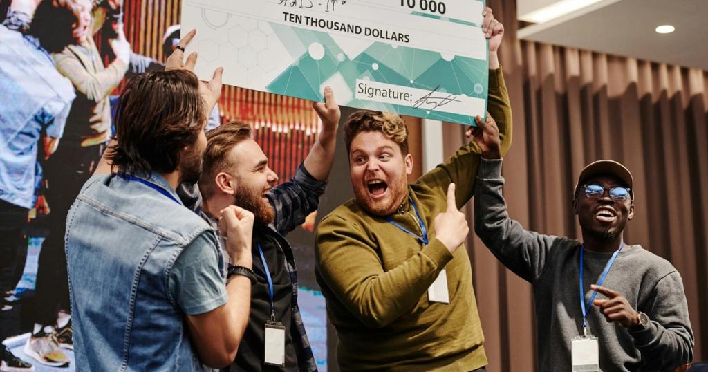 Excited business team celebrates winning a ten thousand dollar prize at a tech conference.