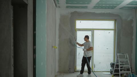A man sprays paint on a wall while renovating an indoor room with professional equipment.