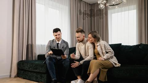 A real estate agent shows a property listing to a couple in a modern living room.