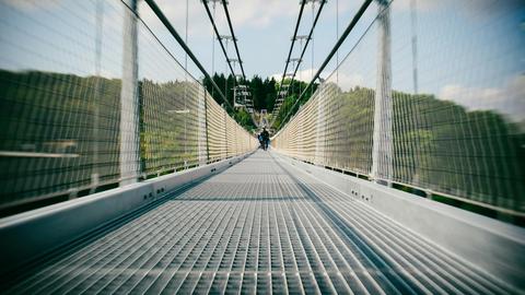 Long suspension bridge with people walking, showcasing modern architecture in a lush, sunny setting.