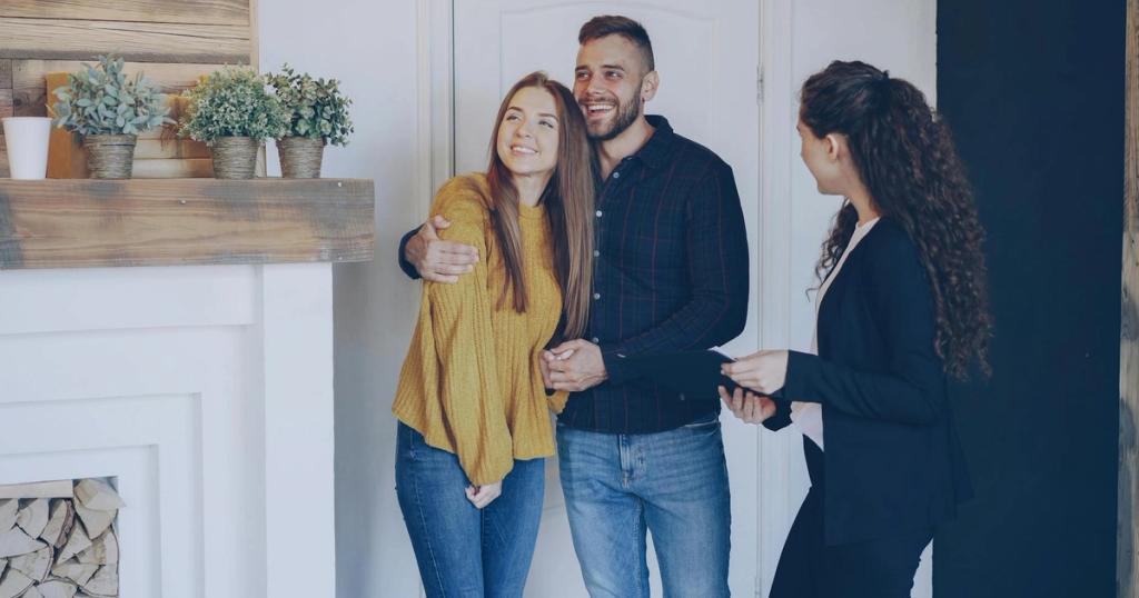 Happy couple meeting with a realtor indoors, discussing property purchase in modern living room.