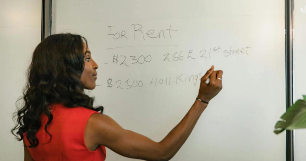 Professional woman writing real estate prices on a whiteboard for rental properties.