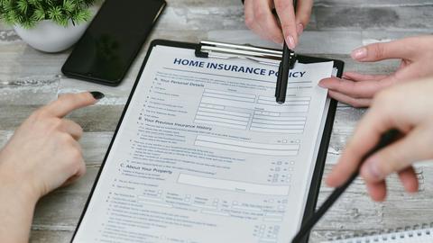 Three individuals collaborating on a home insurance policy document. Elements include a clipboard, notes, and pointing hands.