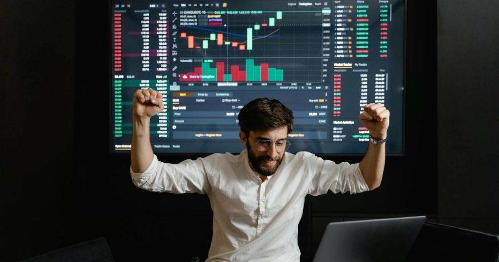 Businessman celebrates stock market success with hands raised in excitement at a trading desk.