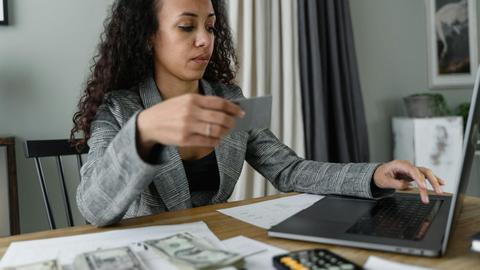Woman using a laptop and managing finances with cash and card on a wooden table indoors.