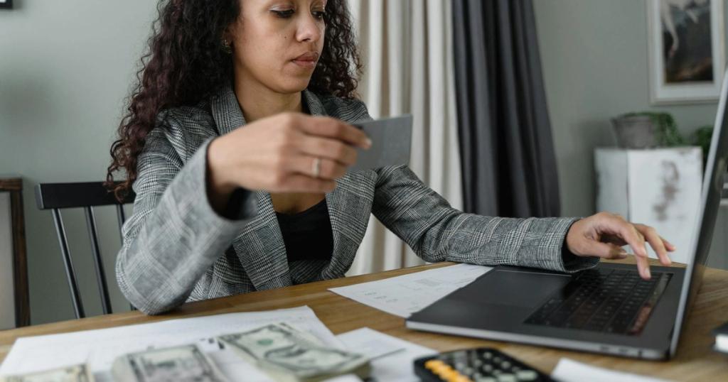 Woman using a laptop and managing finances with cash and card on a wooden table indoors.