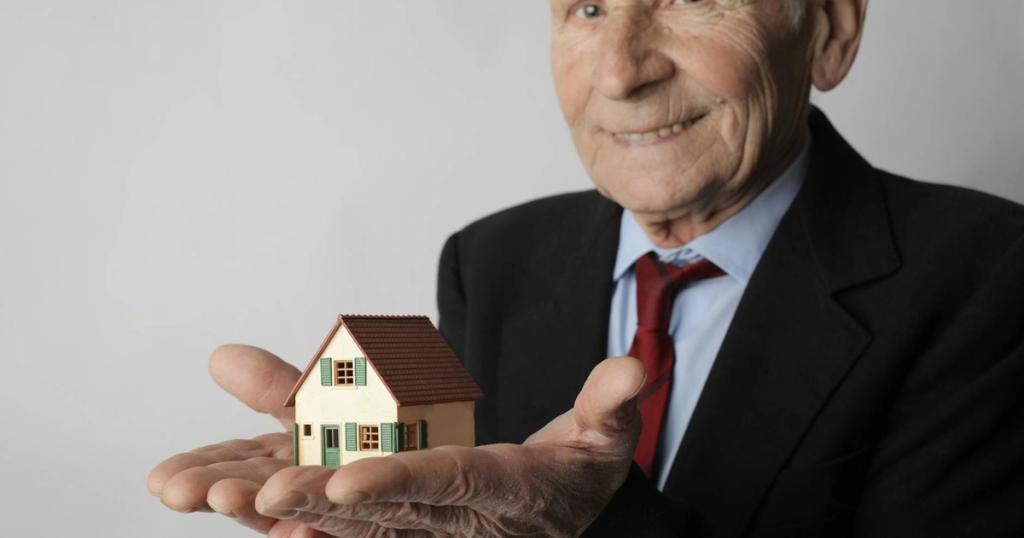 Elderly man in business attire holding a small house model, symbolizing real estate investment.