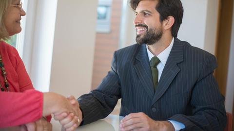 Professional real estate agent sealing a deal with a senior client indoors through a handshake.