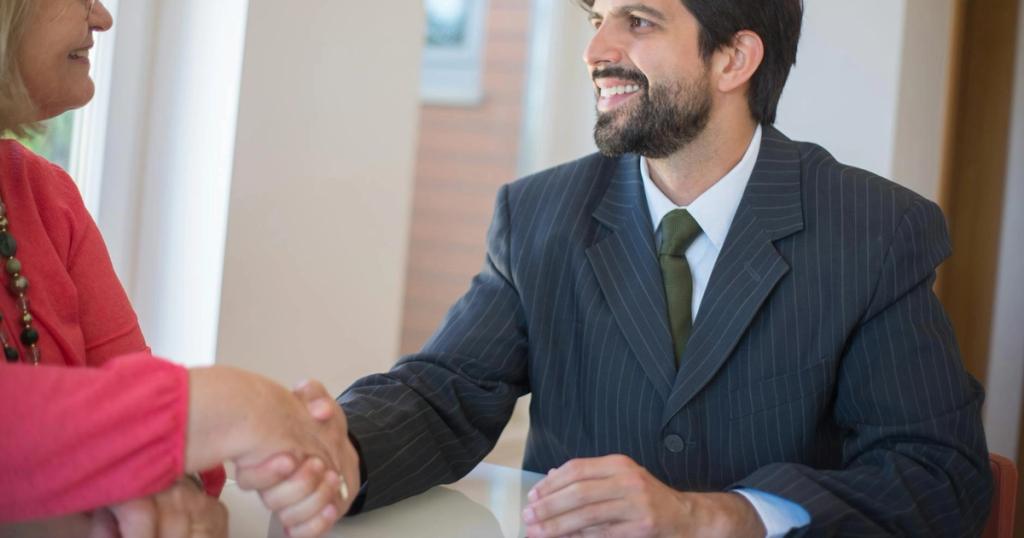 Professional real estate agent sealing a deal with a senior client indoors through a handshake.