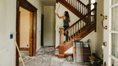 A woman working on home renovation featuring a wooden staircase.