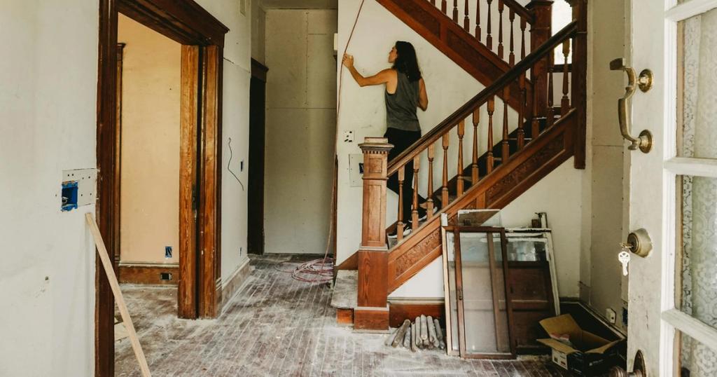 A woman working on home renovation featuring a wooden staircase.