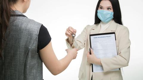 Real estate agent in a face mask hands keys to a client, illustrating safe business practices.