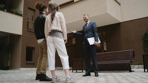 A realtor converses with a couple in a modern apartment courtyard.