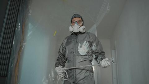 Painter in protective suit with mask and goggles preparing for indoor home renovation.