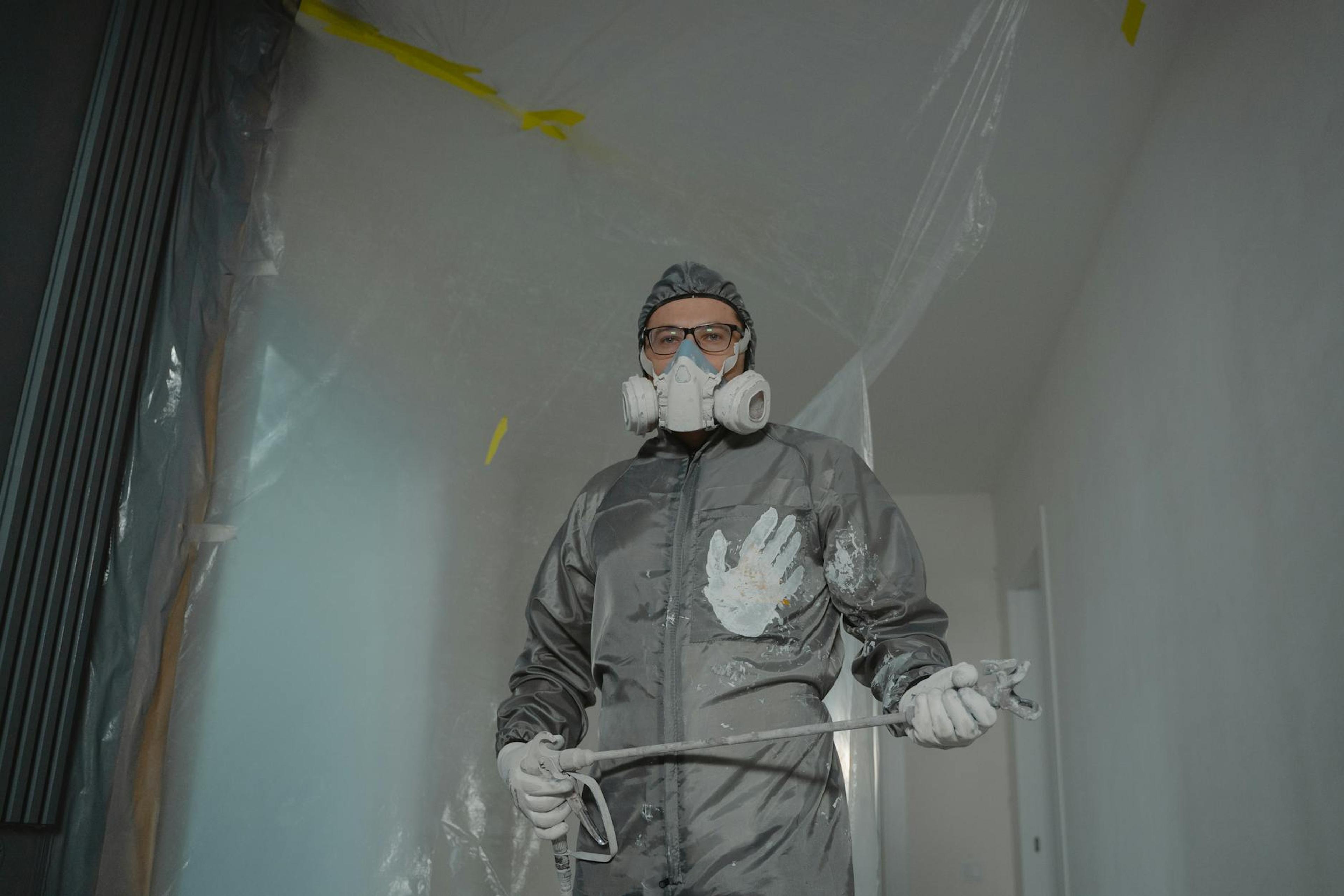 Painter in protective suit with mask and goggles preparing for indoor home renovation.