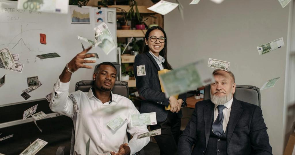 Diverse business team celebrating success with cash raining indoors in office.