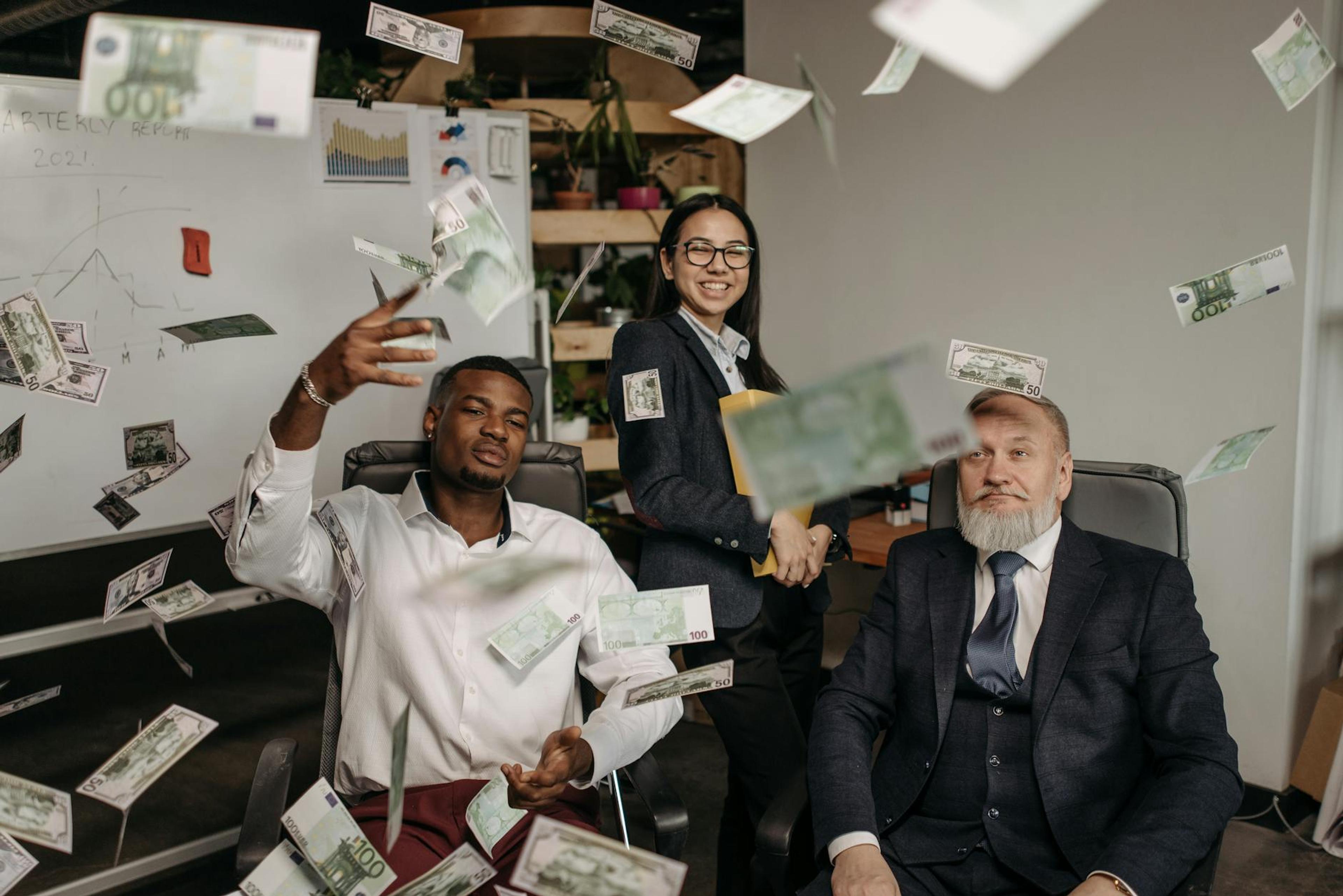 Diverse business team celebrating success with cash raining indoors in office.