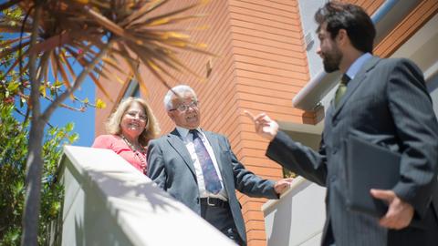 Elderly couple touring a modern home with a real estate agent in sunny Portugal.
