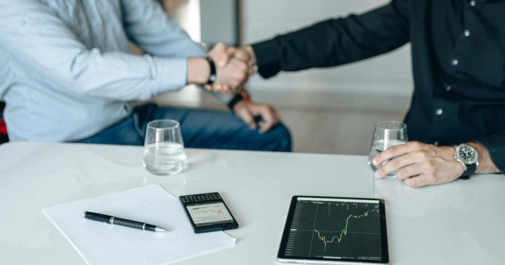 Business meeting with handshake and financial analysis displayed on a tablet.