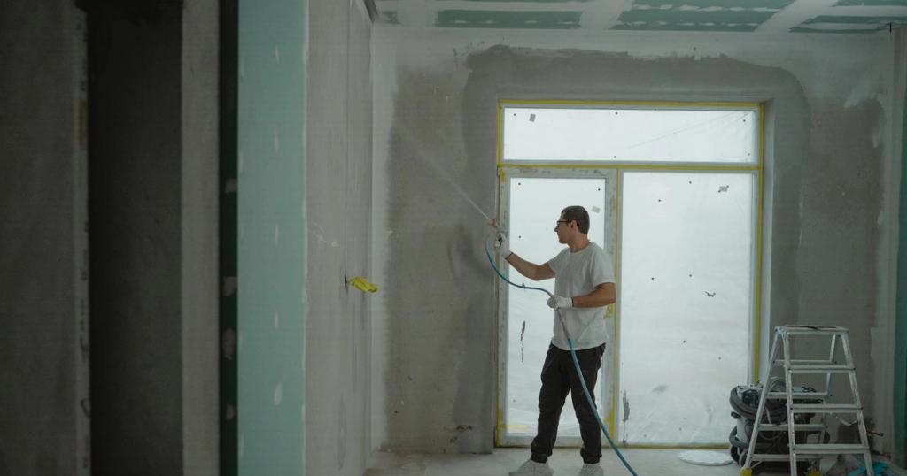 A man sprays paint on a wall while renovating an indoor room with professional equipment.