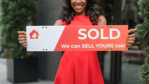 Smiling woman holding a 'Sold' sign, symbolizing successful real estate sales.